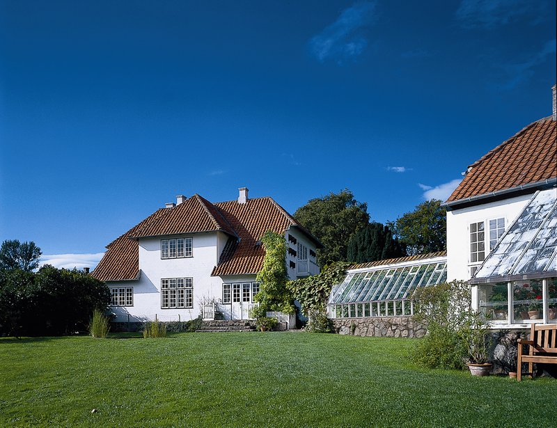 Et stort hvidt hus med en stor have og et drivhus.