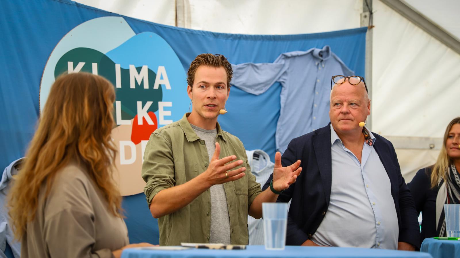 En række paneldebattører står på scenen med Klimafolkemødets logo i baggrunden.