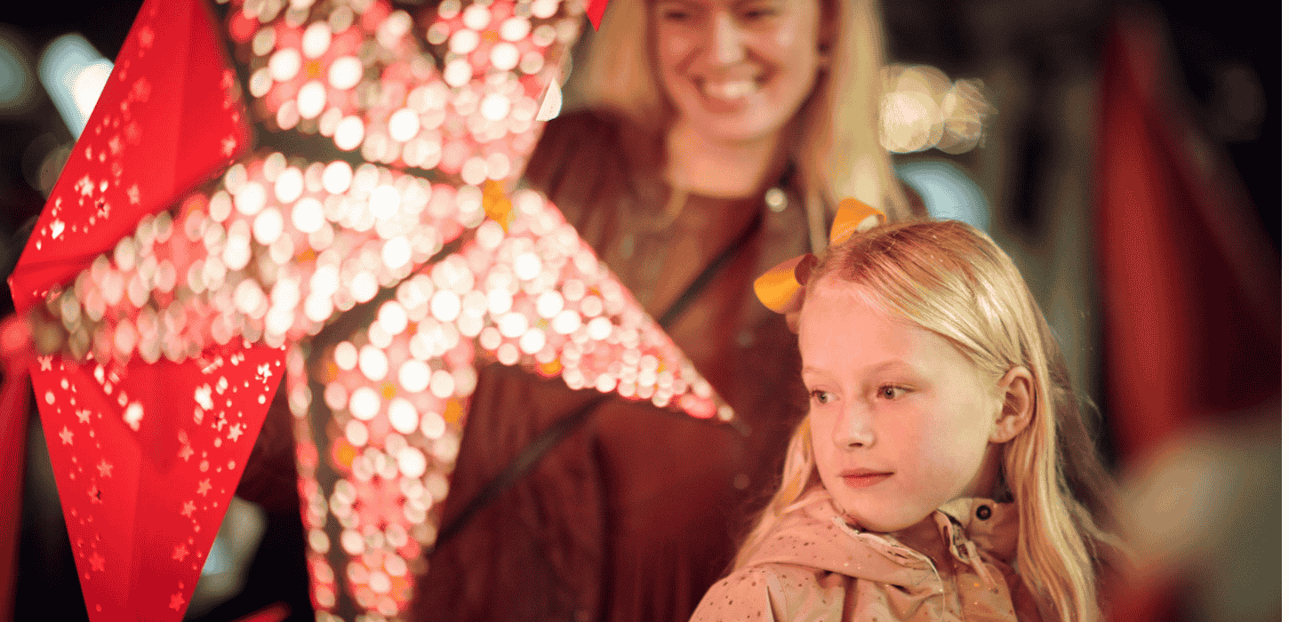 En lille pige og kvinde går på julemarked med lysende julestjerner