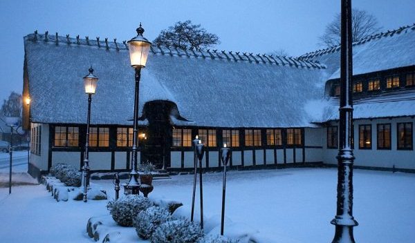 Sneklædt gammeldags hus med stråtækt tag og bindingsværk og lygtepæle foran