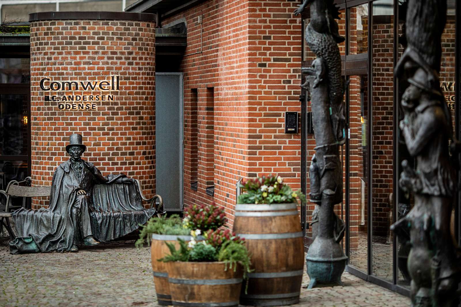 Indgangsparti ved hotel af røde mursten med gamle tønder og en statue af H. C. Andersen foran
