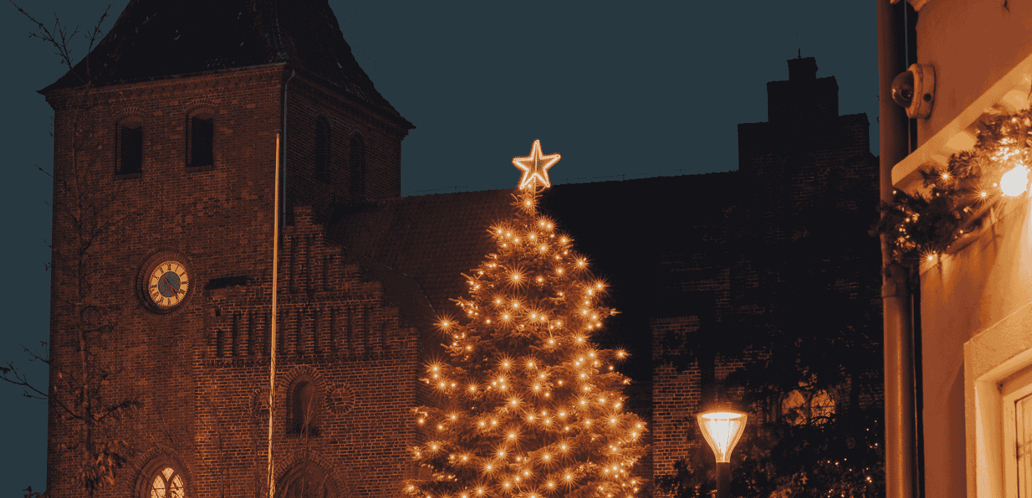 Højt juletræ med julebelysning og en kirke i baggrunden 