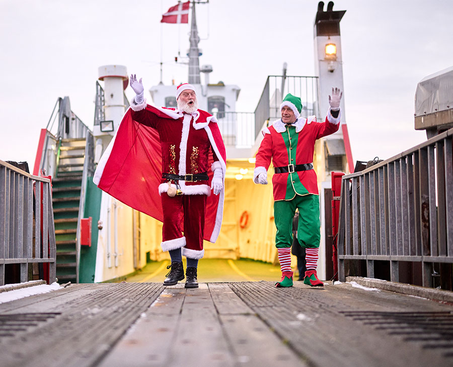 Julemandsudklædt man går i land fra en færge sammen med en nisseklædt person