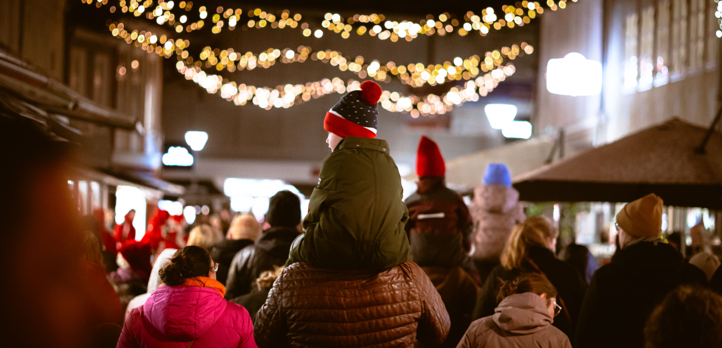 Et parn sidder på sin forælders skuldre om aftenen i en gade oplyst af julebelysning