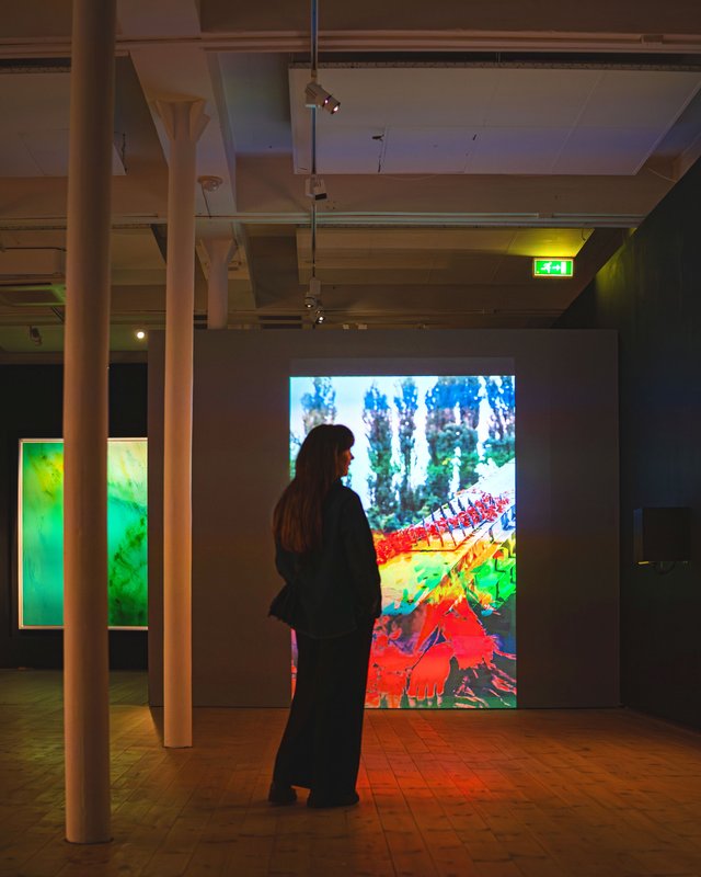 En ung kvinde står foran et lysende stykke kunst i en hal med dæmpet belysning