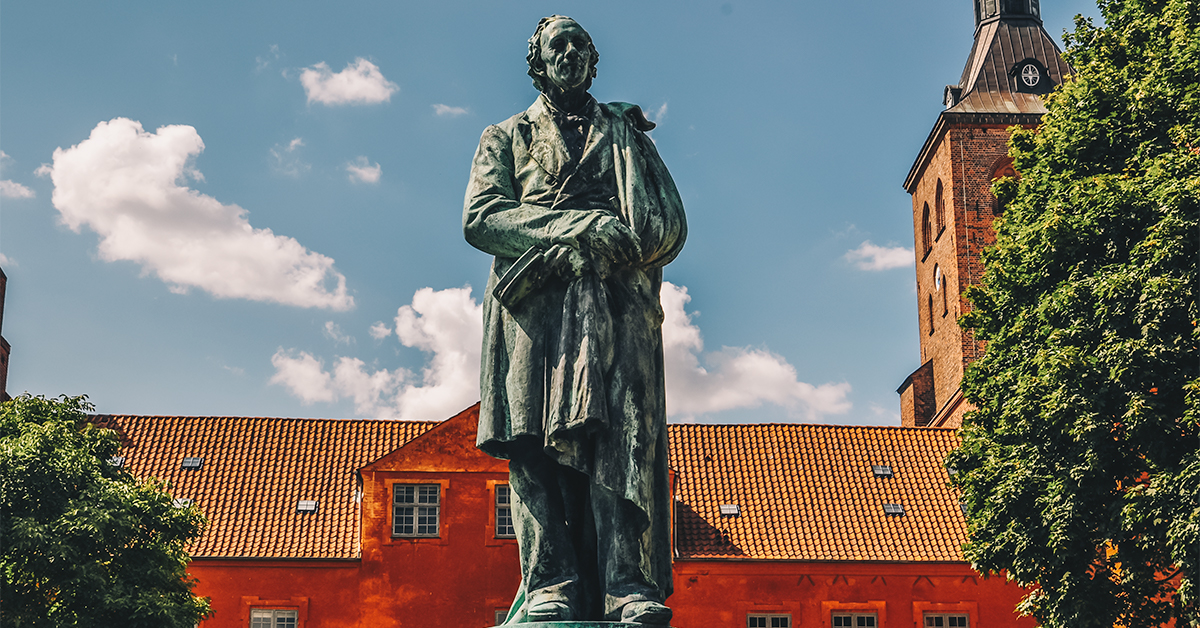 En statue af H. C. Andersen med kirke og blå himmel i baggrunden