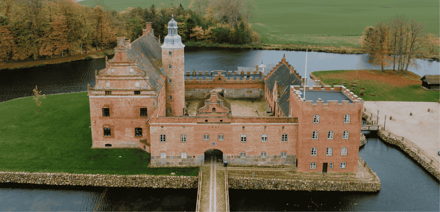 Et slot med voldgrav, slotstårn og gårdhave i efteråret med gyldengrønne træer