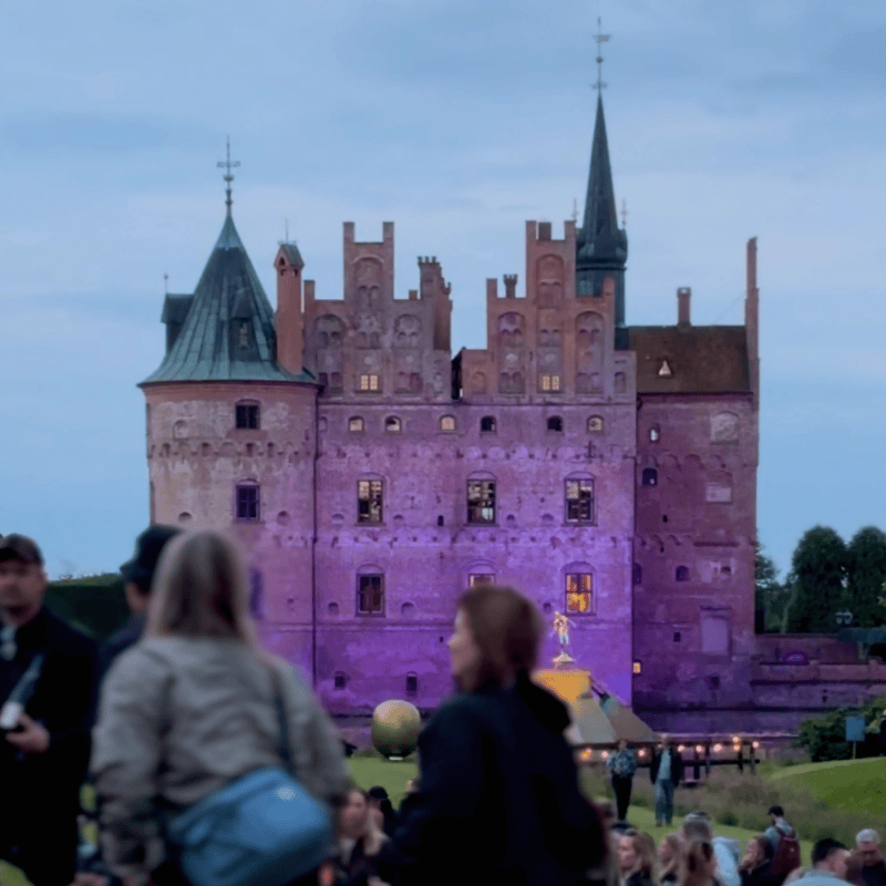 Egeskov Slot oplyst i lilla farver med festivalgængere foran