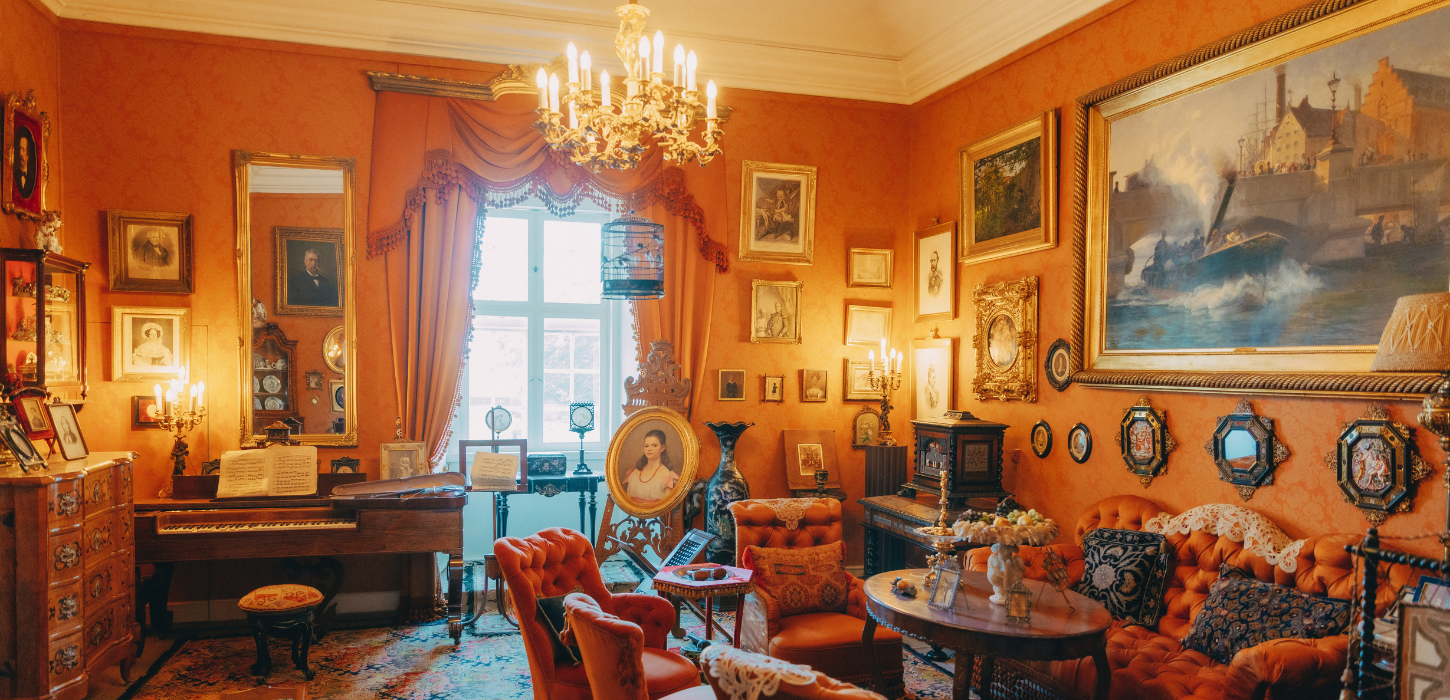 En stor dagligstue indrettet i renæssancestil med orangetonet interiør, lysekrone, tunge gardiner, stuk og massive møbler