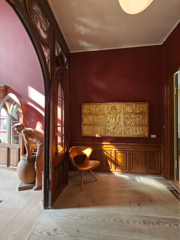 Et bordeaux indgangsrum med et kunstværk i guld hængende på væggen og en læderstol i hjørnet