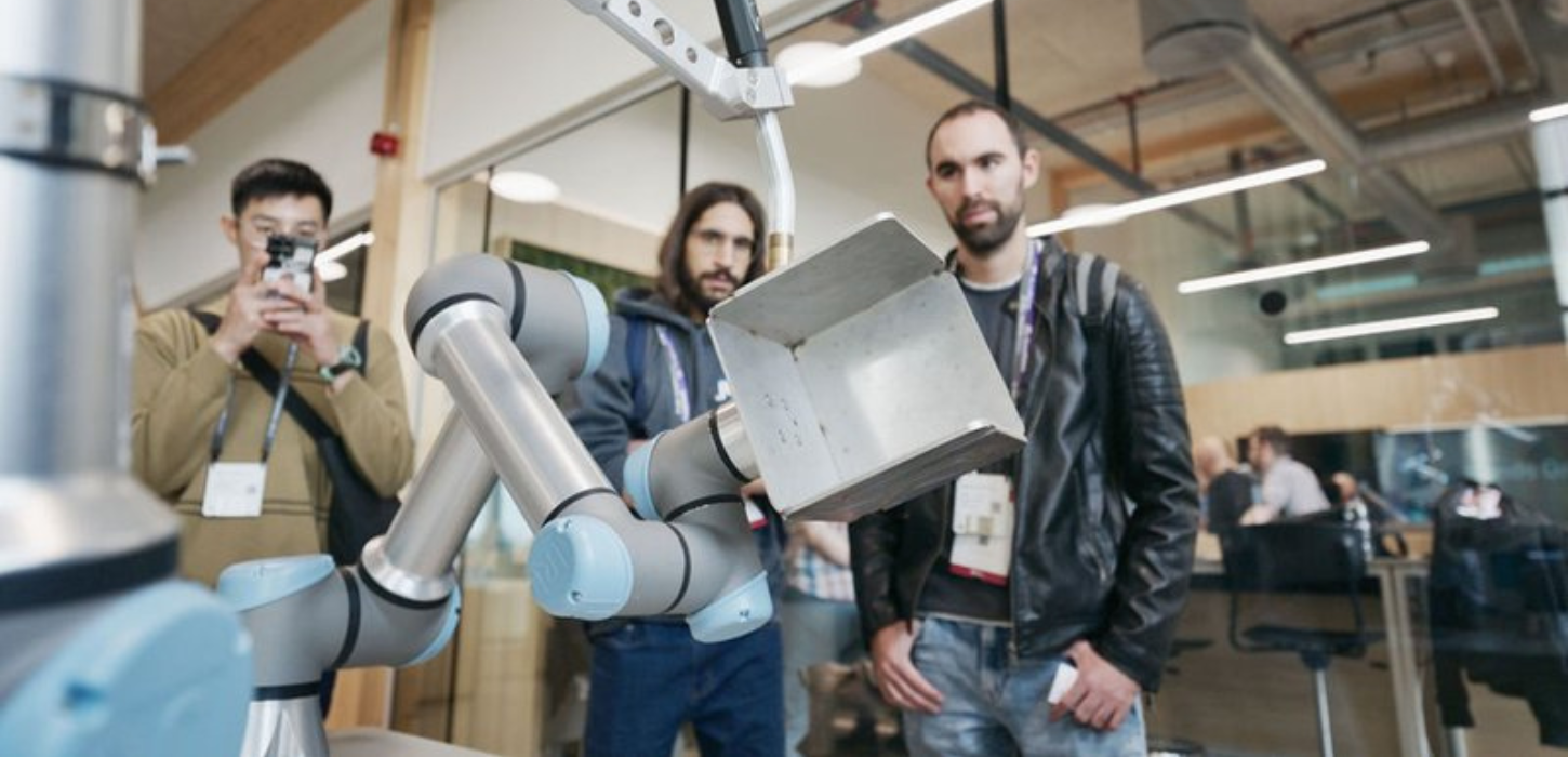 Tre mænd står og ser på en robotarm.