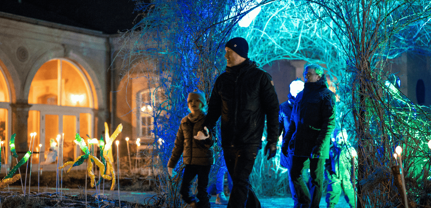 En familie går udendørs iklædt vinterbeklædning, og omkring dem er der lys i forskellige farver