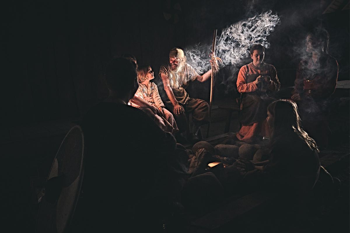 Et dunkelt rum oplyses af en enkelt solstråle, der oplyser en lille flok vikingeklædte mennesker 