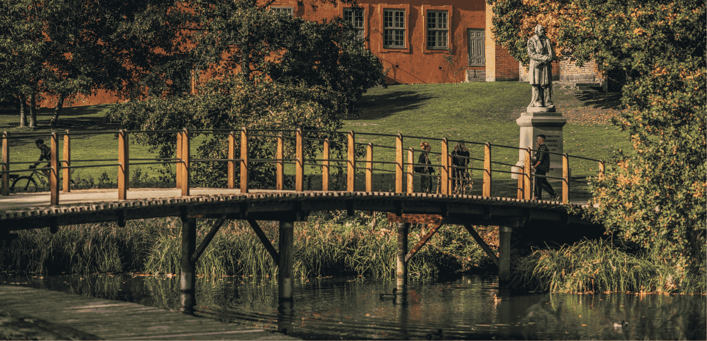 En park med en bro over en å med græs og orange murværk i baggrunden