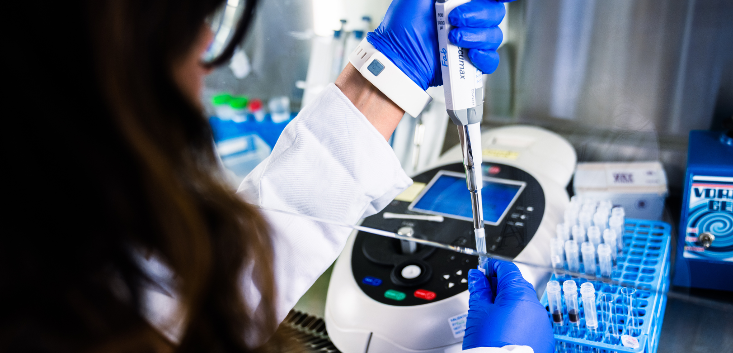 Hænder med blå engangshandsker injicerer i reagensglas