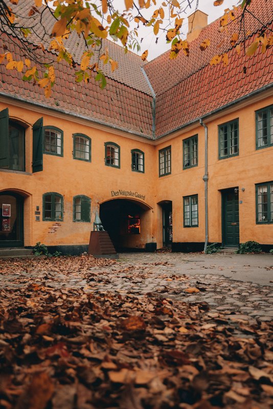 En gulmalet ældre bygning i efteråret med gule og orange blade i gårdhaven