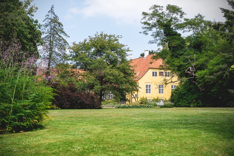 Et gult gods med træer og buske og græsplæne foran