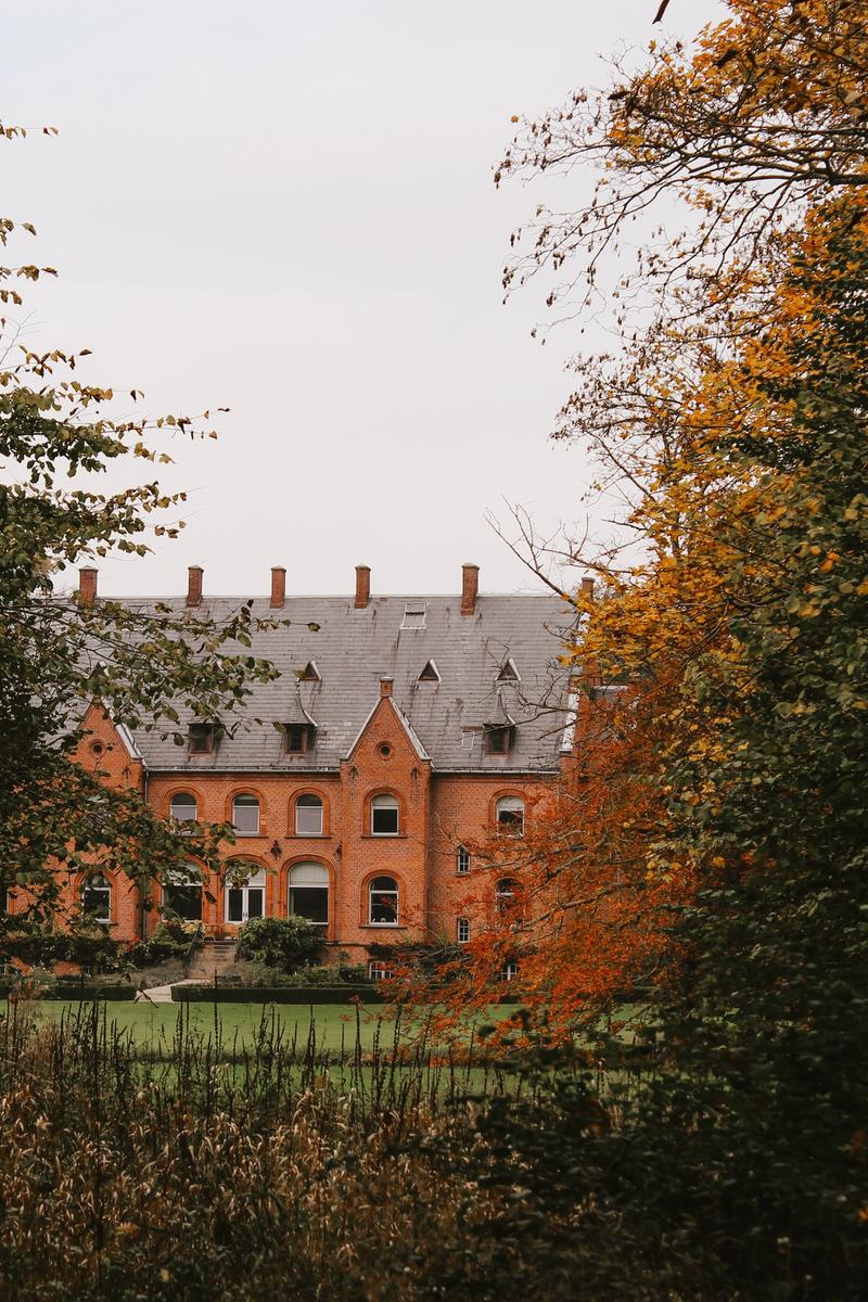 Et rødmuret gods indrammet af efterårsblade på en gråvejrsdag