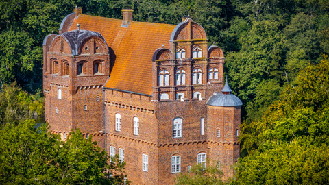 Et slot i røde mursten omringet af grøn skov