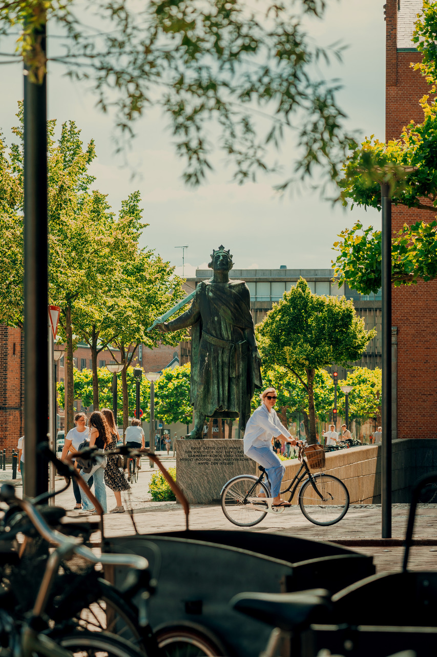 En statue står midt på en cykelsti hvor en cyklist cykler forbi