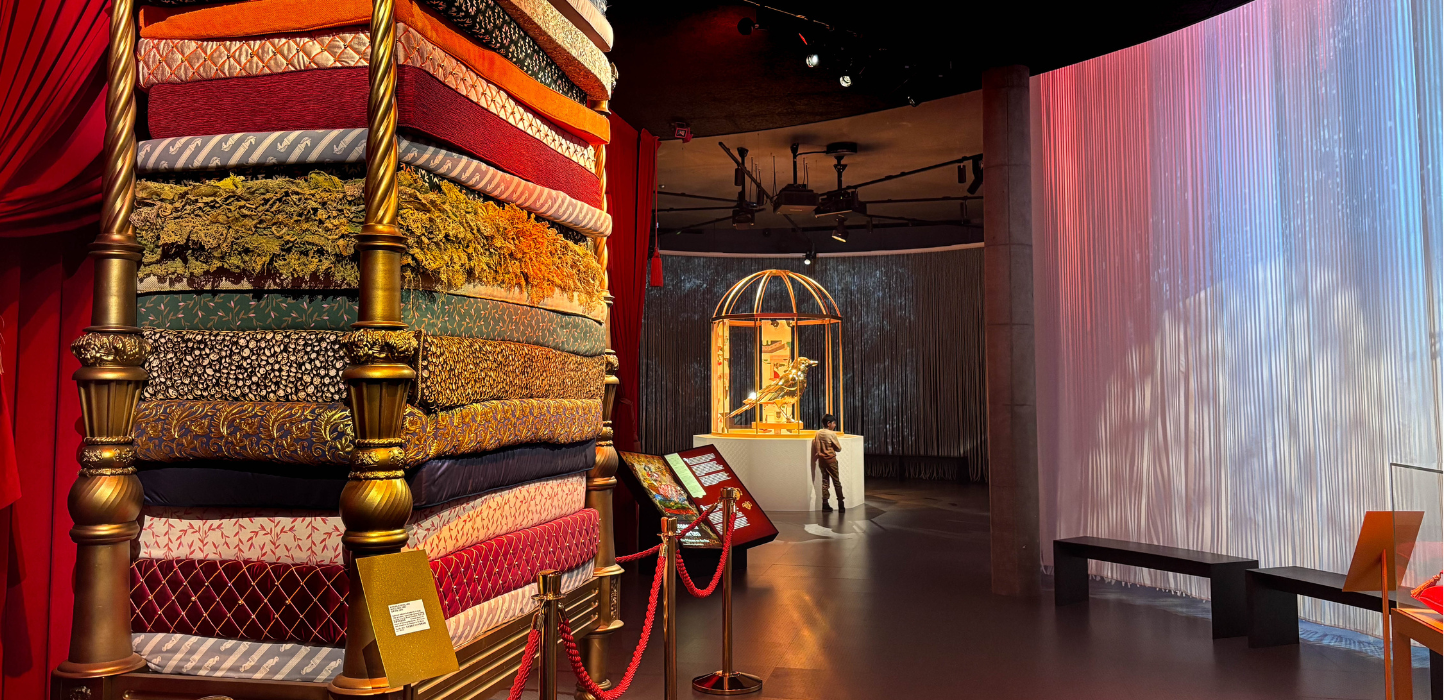 En farverig udstilling bestående af en seng med et tårn af forskelligfarvede madrasser, et guldfuglebur i midten og farverigt vægbeklædning