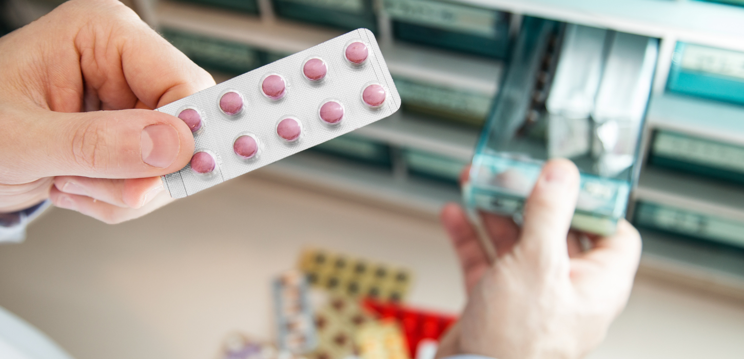 Hånd holder blisterpakke med piller, der er taget ud af medicinskab