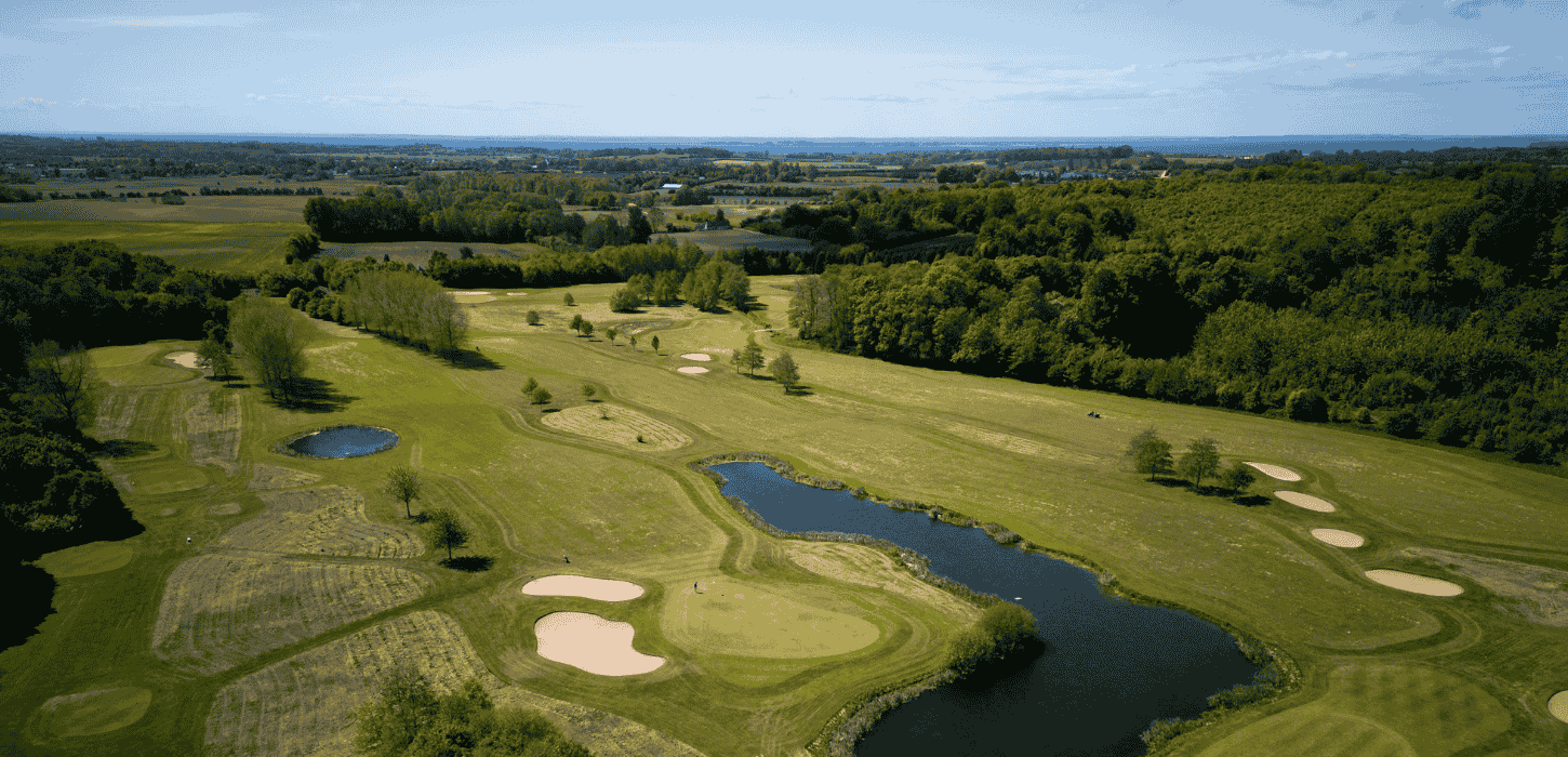 Grøn golfbane se fra luften med sandbanker, sø og omkransende træer 