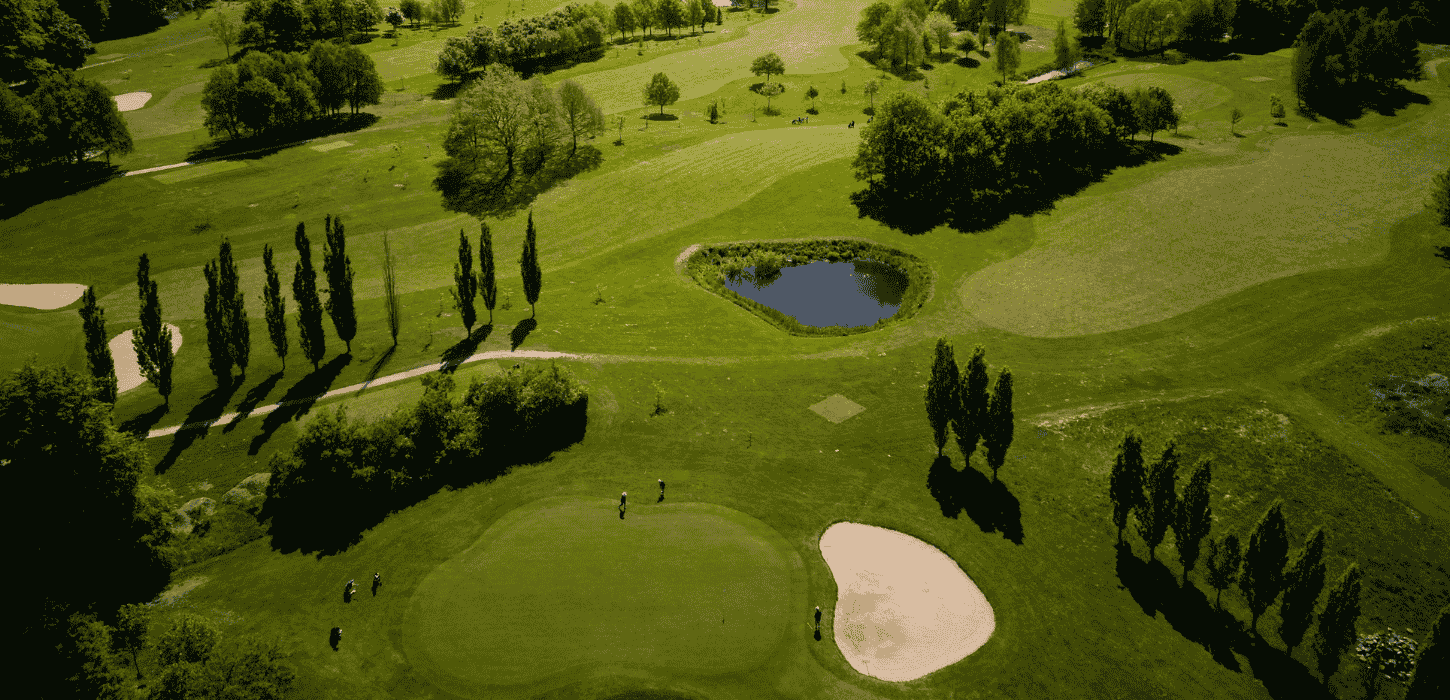 Dronebilleder af en grøngræsset golfbane med sandbanker, søer, træer og golfspillere