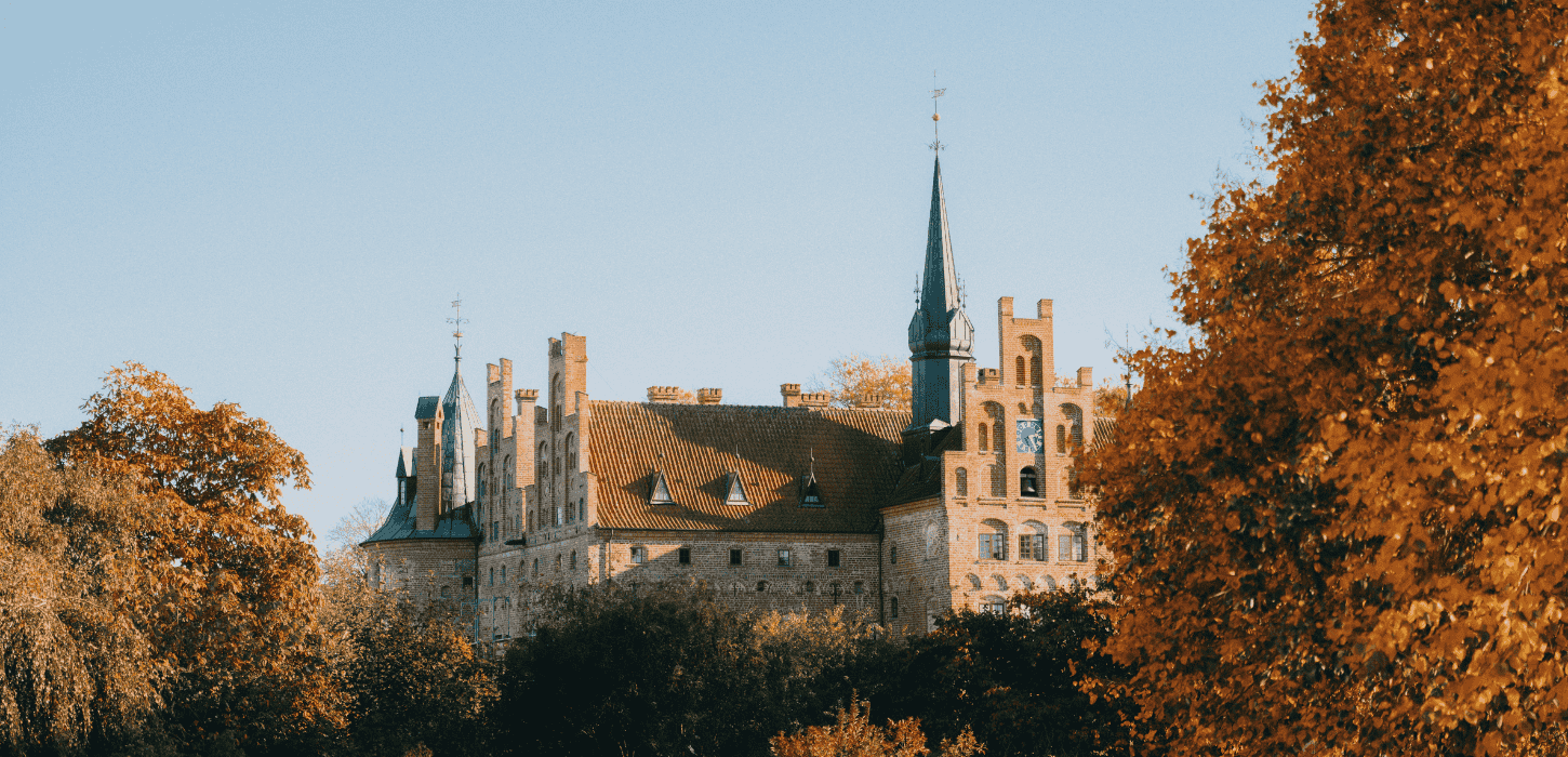 Et slot med spir ses med efterårsfarvede blade i forgrunden