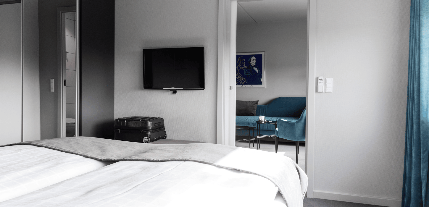 Hotelværelse med dobbeltseng, tv på væggen og et tilstødende stue-rum
