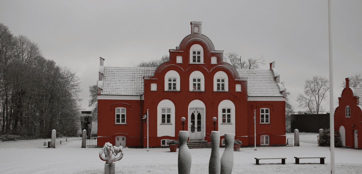 En rød herregård iklædt sne med skulpturer foran 