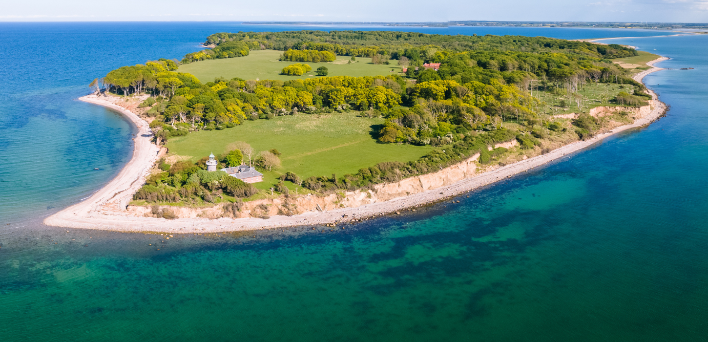 Dronefoto af en ø omringet af havet og som ikke er større end et par kvadratkilometer, med hvide kyster og grøn skov. 