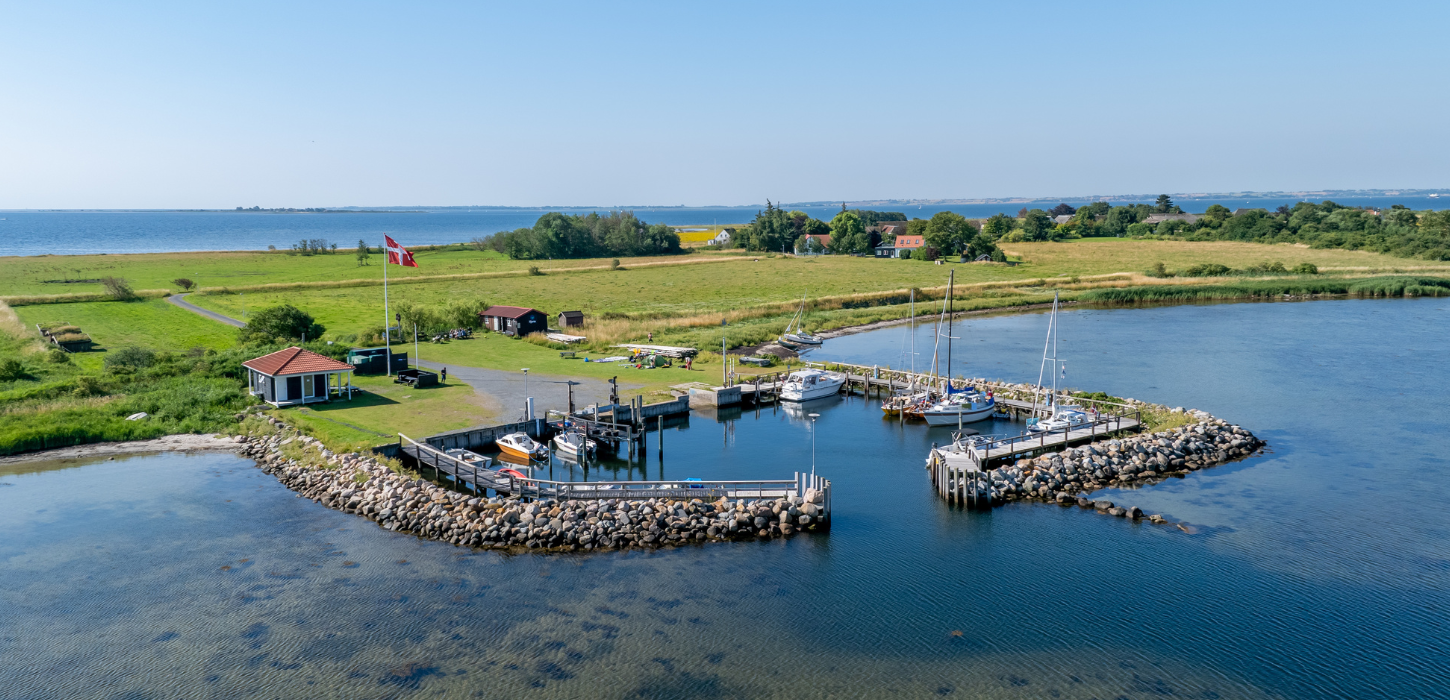 Dronebillede af Hjortø. Øen er både omgivet af blåt vand og himmel. 