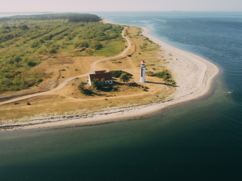 Et dronefoto af en kyst med et fyrtårn og blå hav