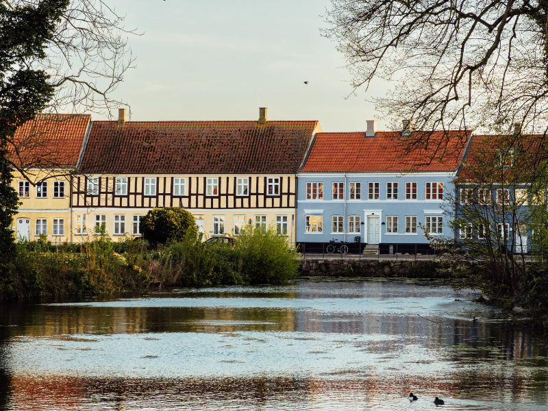 Nogle farverige bindingsværkfacader ligger i baggrunden af en stille sø på en forårsdag