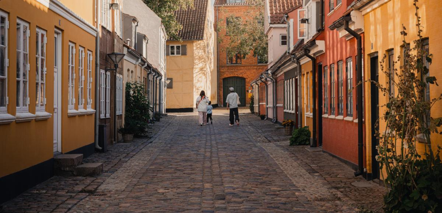 Tre personer går ned ad brostensbelagt gade med farverige husfacader