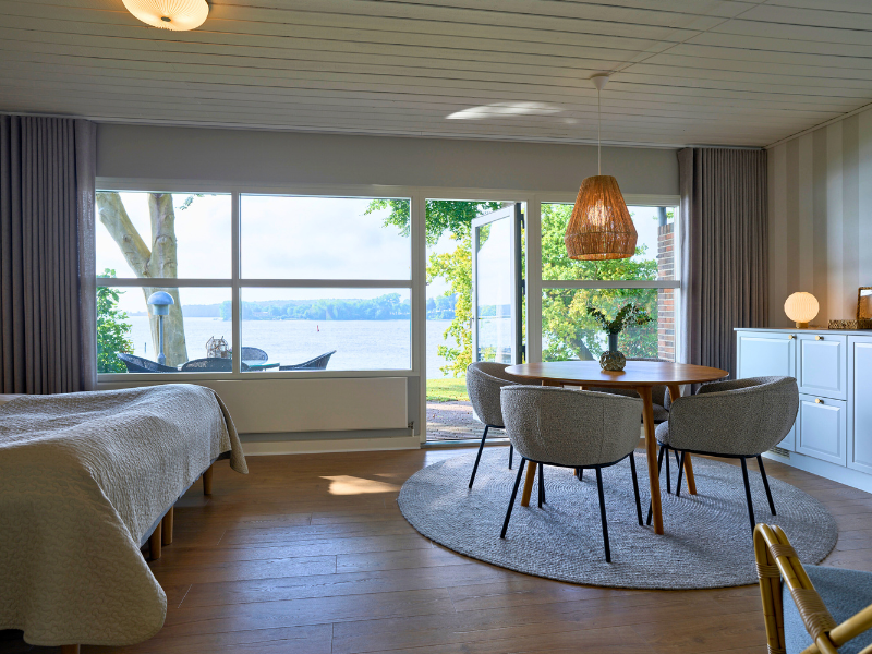 Et værelse set indefra med udsigt til Svendborg Sund, seng og borde og stole og naturfarvet indretning