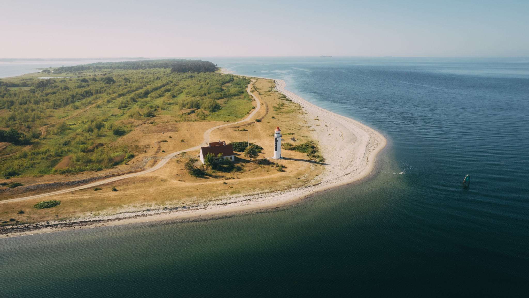 Dronefoto af en hvid sandstrand på en halvø med hav omkring og et hvidt fyrtårn