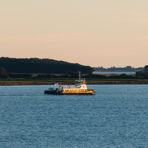 En færge sejler i roligt hav en sensommeraften med gyldent lys i horisonten