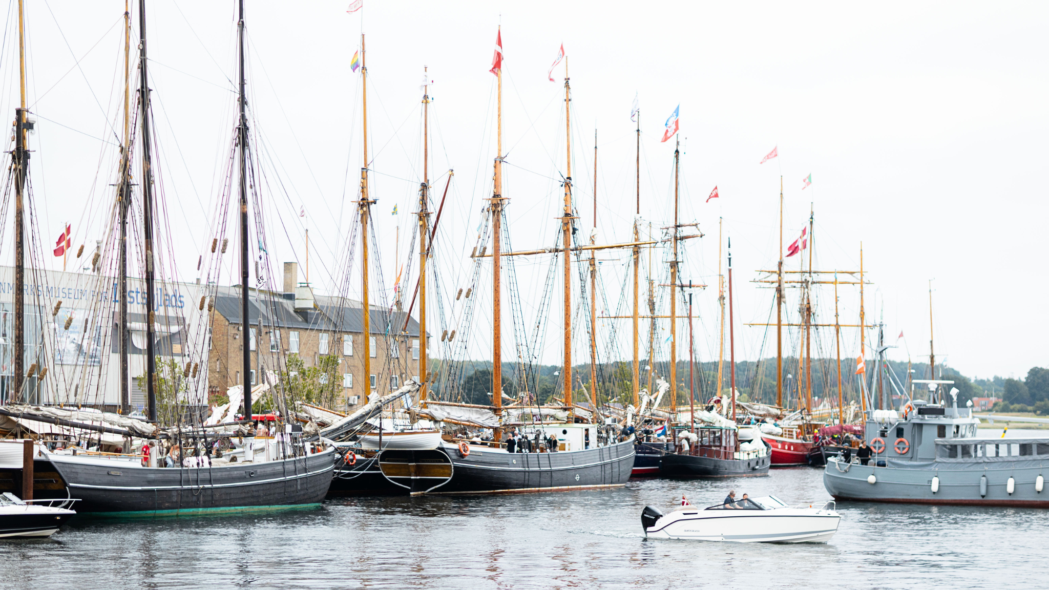 En samling af træskibe er docket i havnen med bølger der skvulper blidt mod skroget.