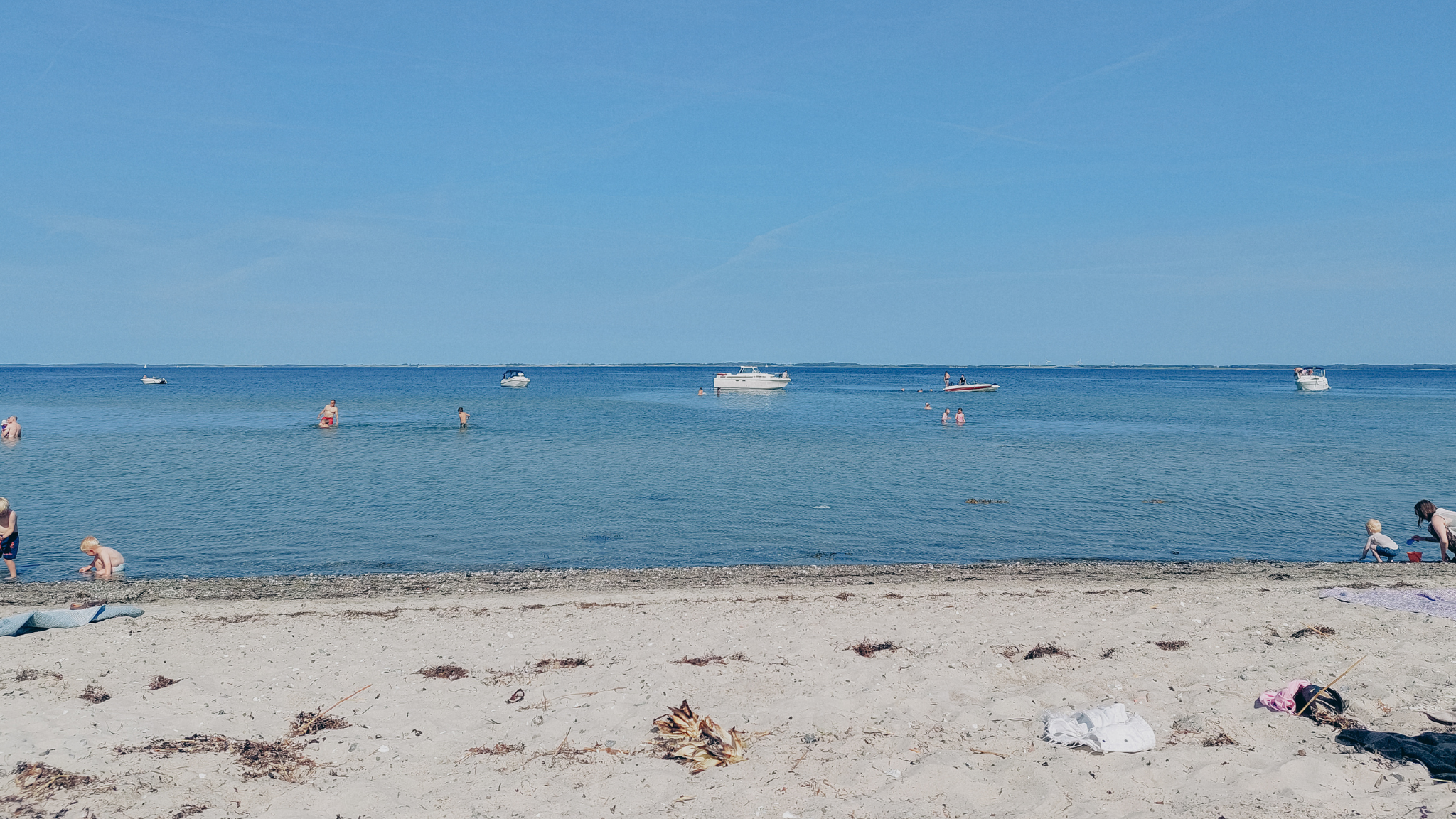 En hvid sandstrand med badende gæster og et par skibe i horisonten