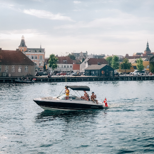En speedbåd med passagerer glider gennem Svendborg Sund under en klar sommerhimmel.