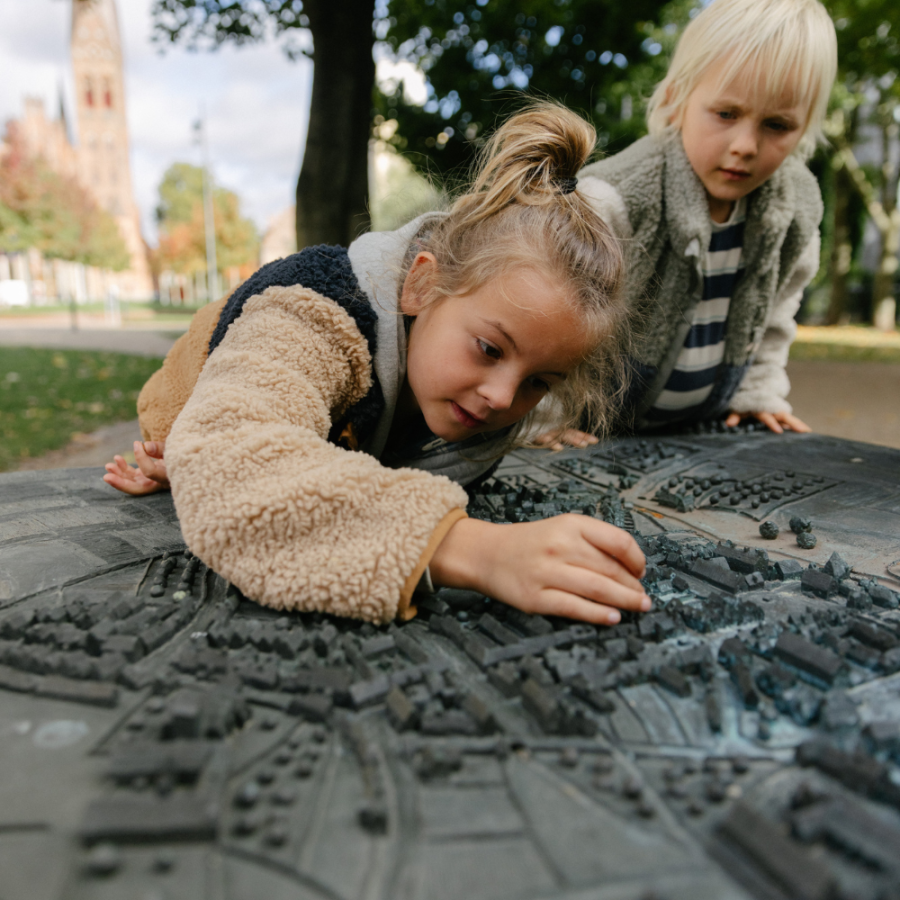 To børn hænger ind over en bronzestatue, der viser hvordan Odense så ud i vikingetiden. 
