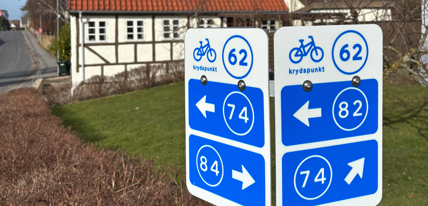 Cykelnetskilte på Langeland med bindingsværkshus i baggrunden