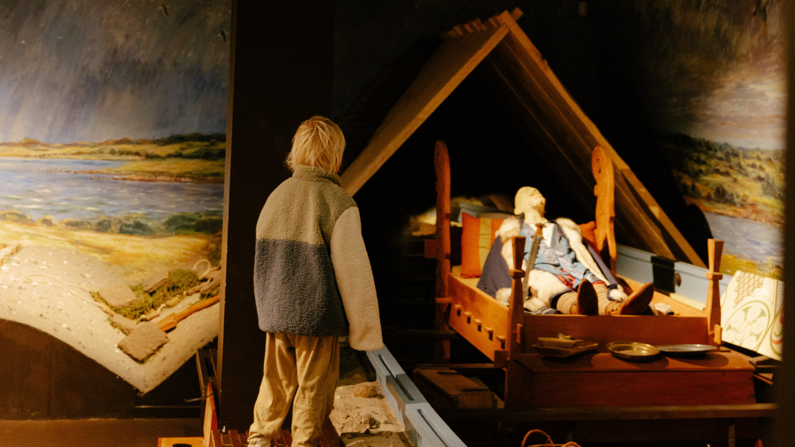 En dreng kigger på en udstilling, der består af et replikeret vikingeskib med diverse rekvisitter