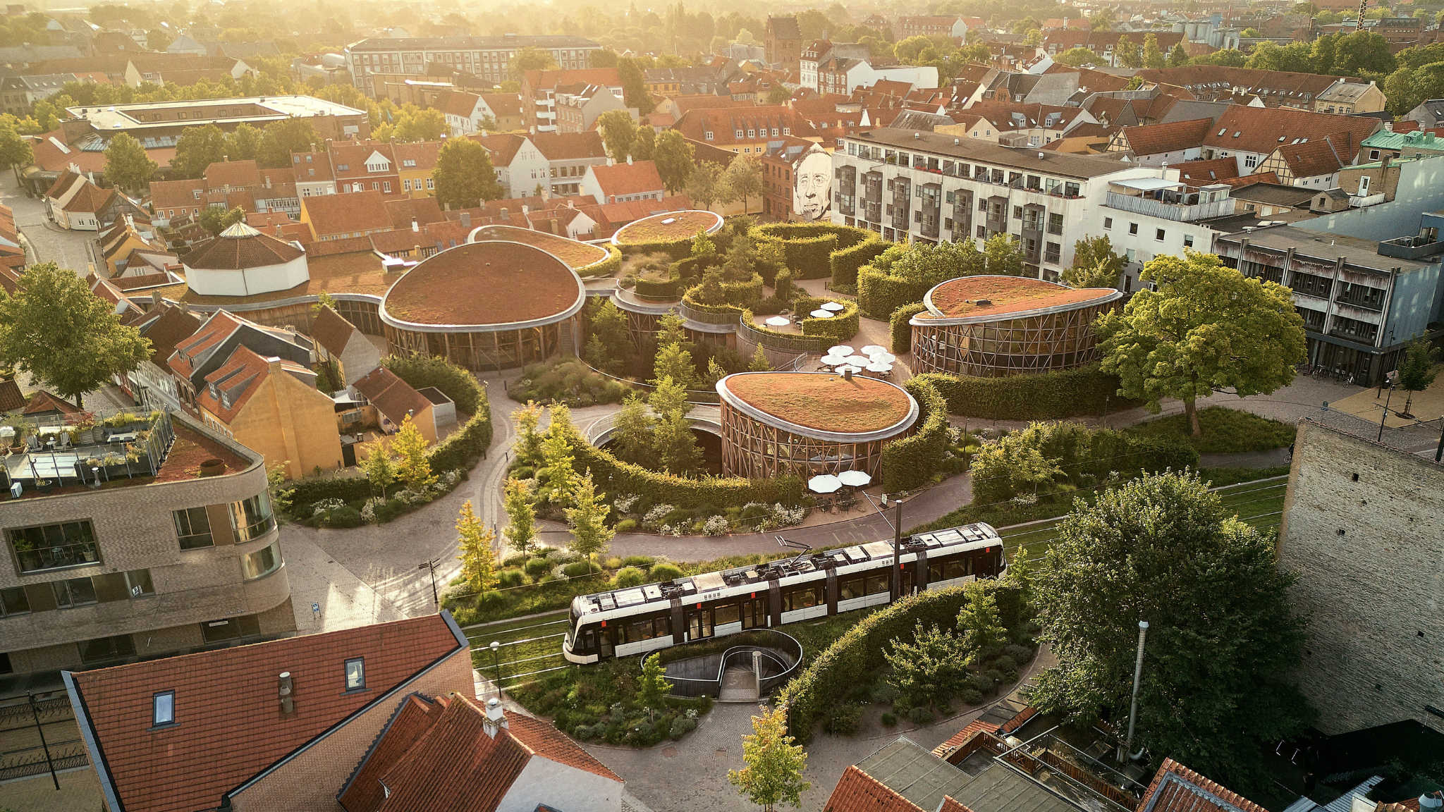 Dronefoto af området i Odense omkring H. C. Andersens Hus, som er et museum bestående af runde bygninger med mostag og træfacader. 