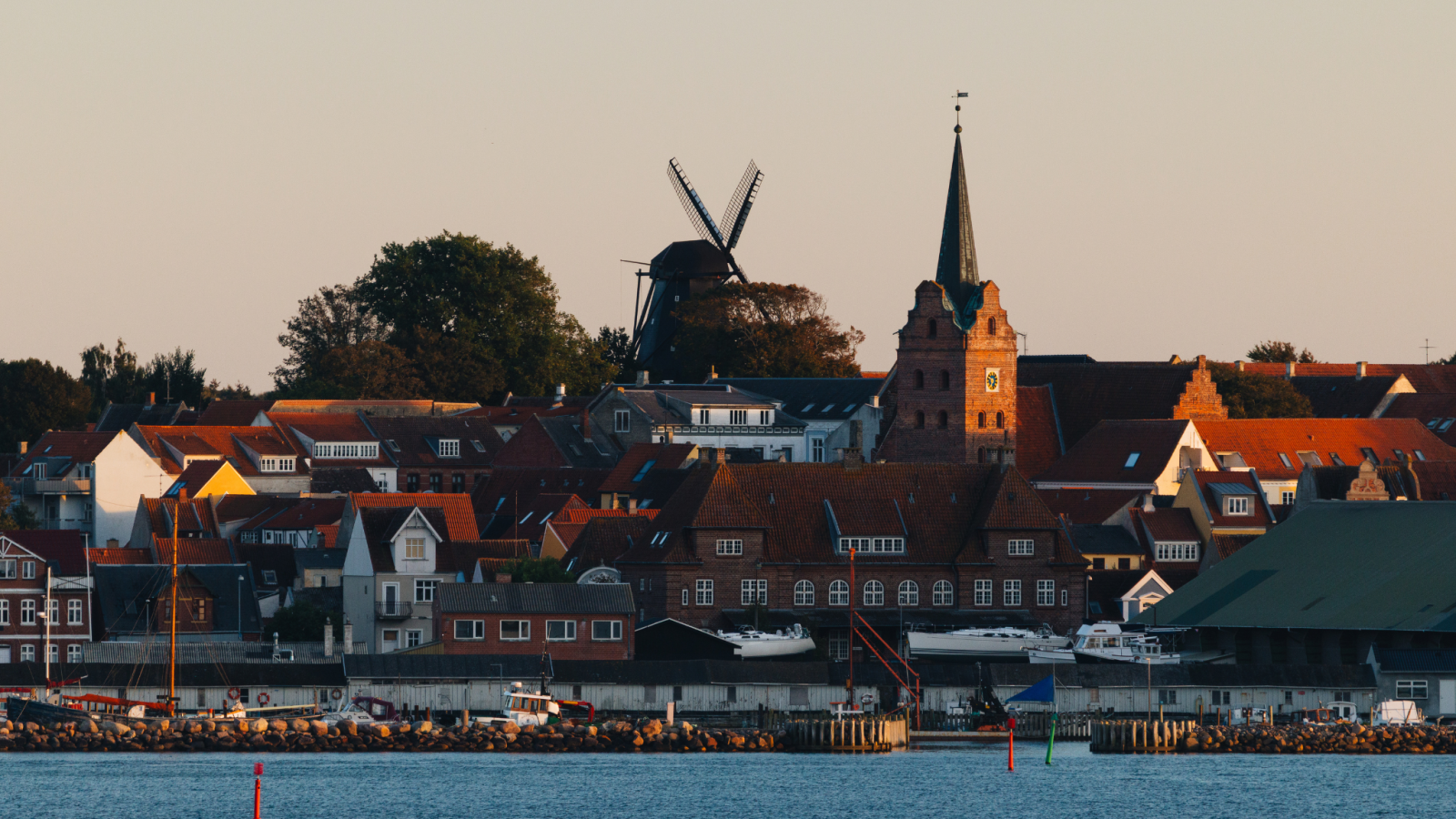 Købstaden Rudkøbing set fra havet. En række gamle boliger med klokketårn og mølle i baggrunden. 