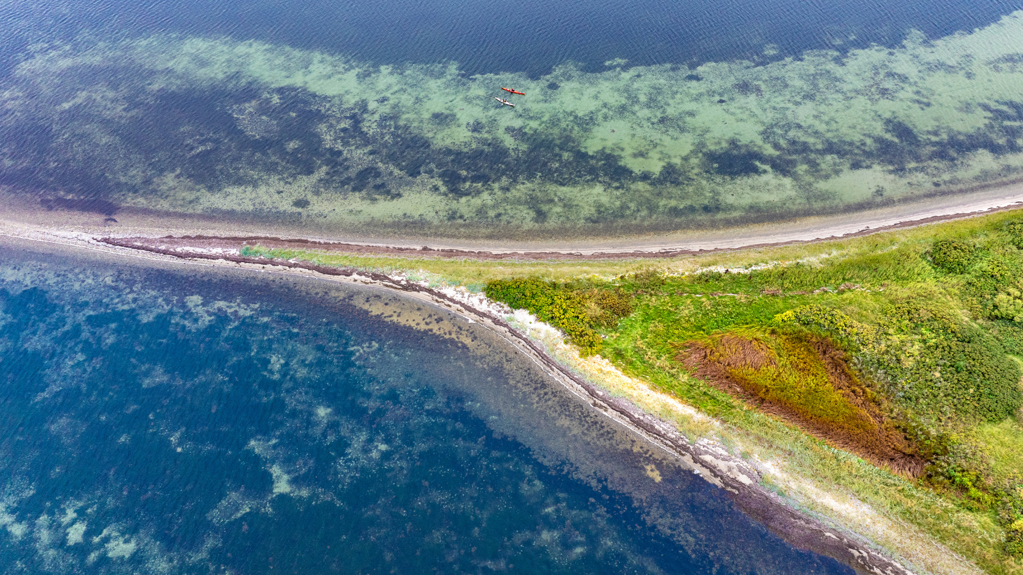 Et dronefoto af tippen af en ø, hvor der er ud for kystlinjen er to kajakker. 