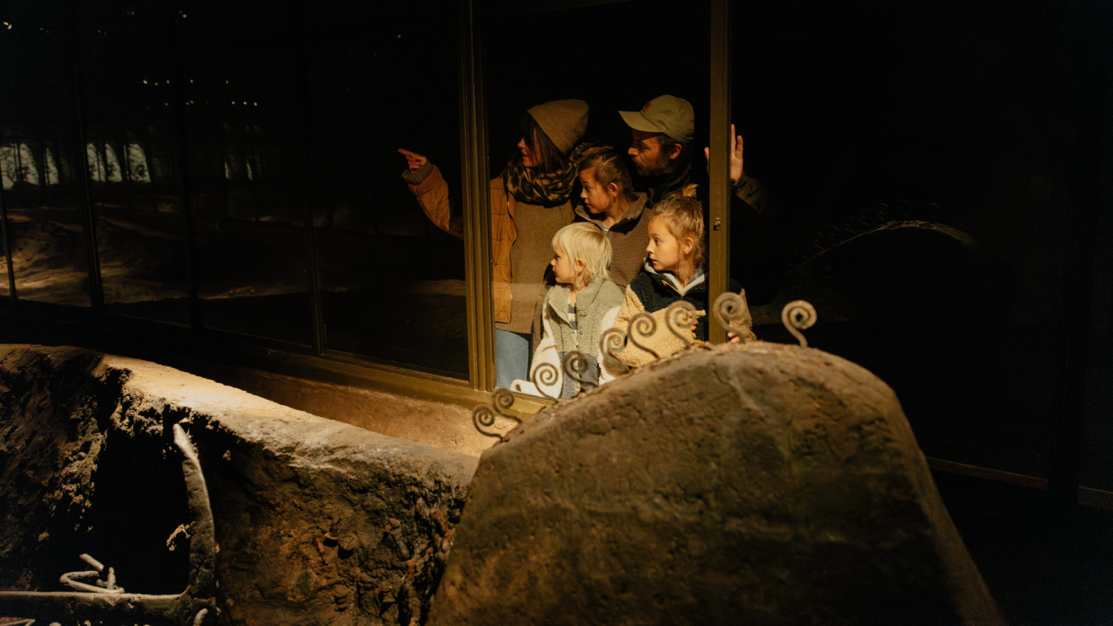 En familie på fem står og kigger ind i en montre, hvori et udgravet vikingeskib er udstillet. 