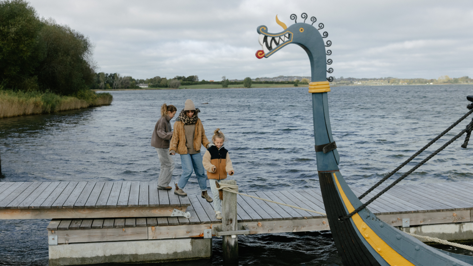 En gruppe mennesker på en dok ved en replika af et vikingeskib, der ser glade ud og nyder deres tid sammen.